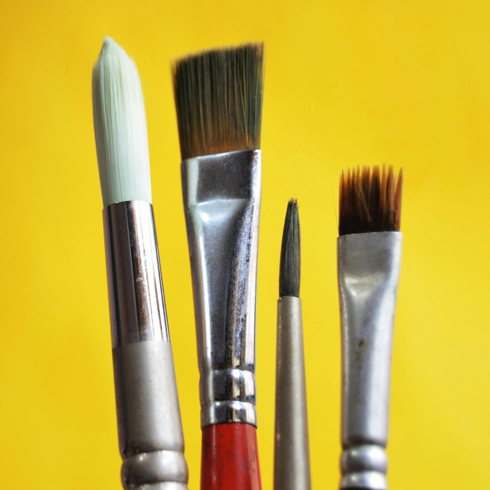 Close-up of varied paint brushes against a bright yellow backdrop.