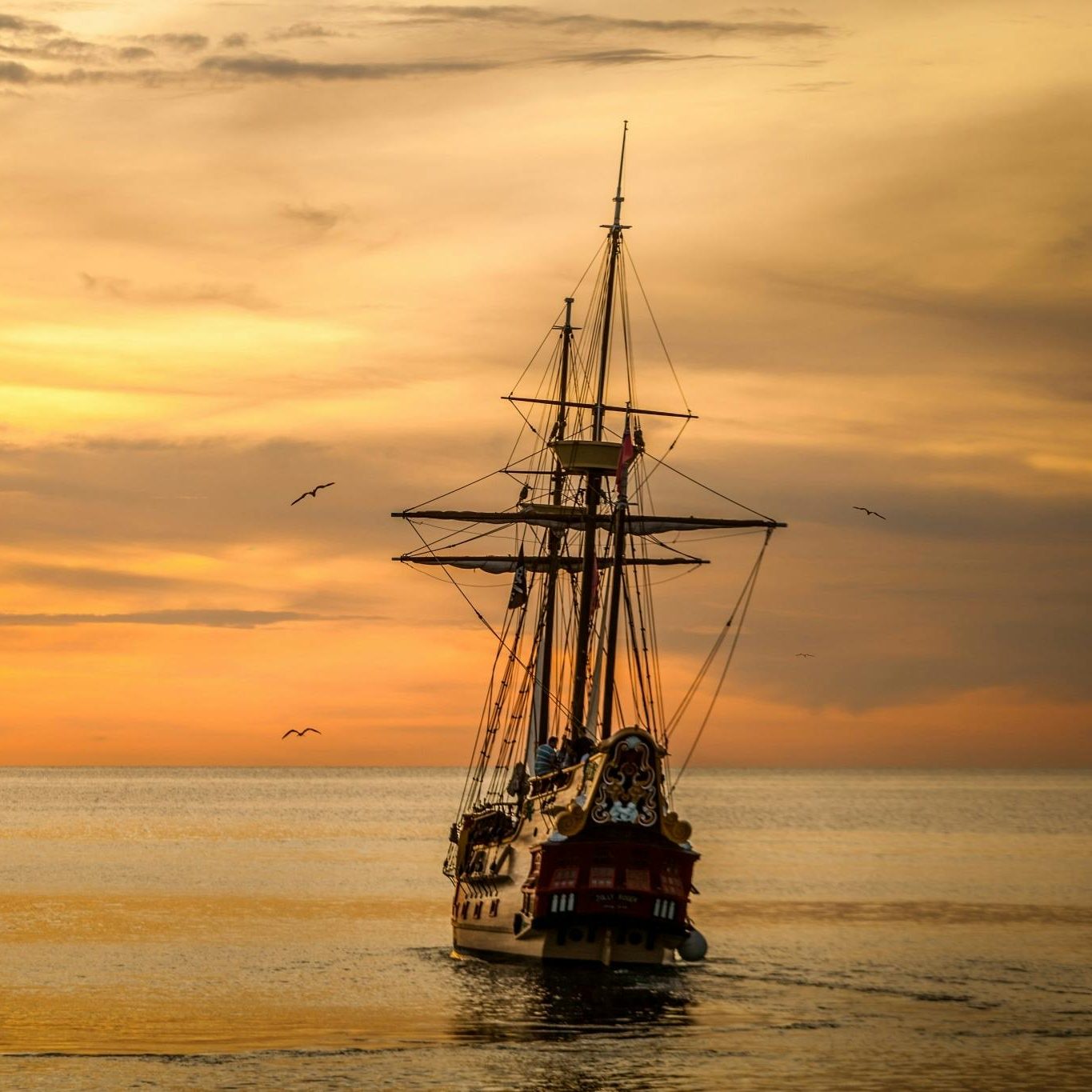 A majestic pirate ship sails into the serene waters at sunset, casting a dramatic silhouette.
